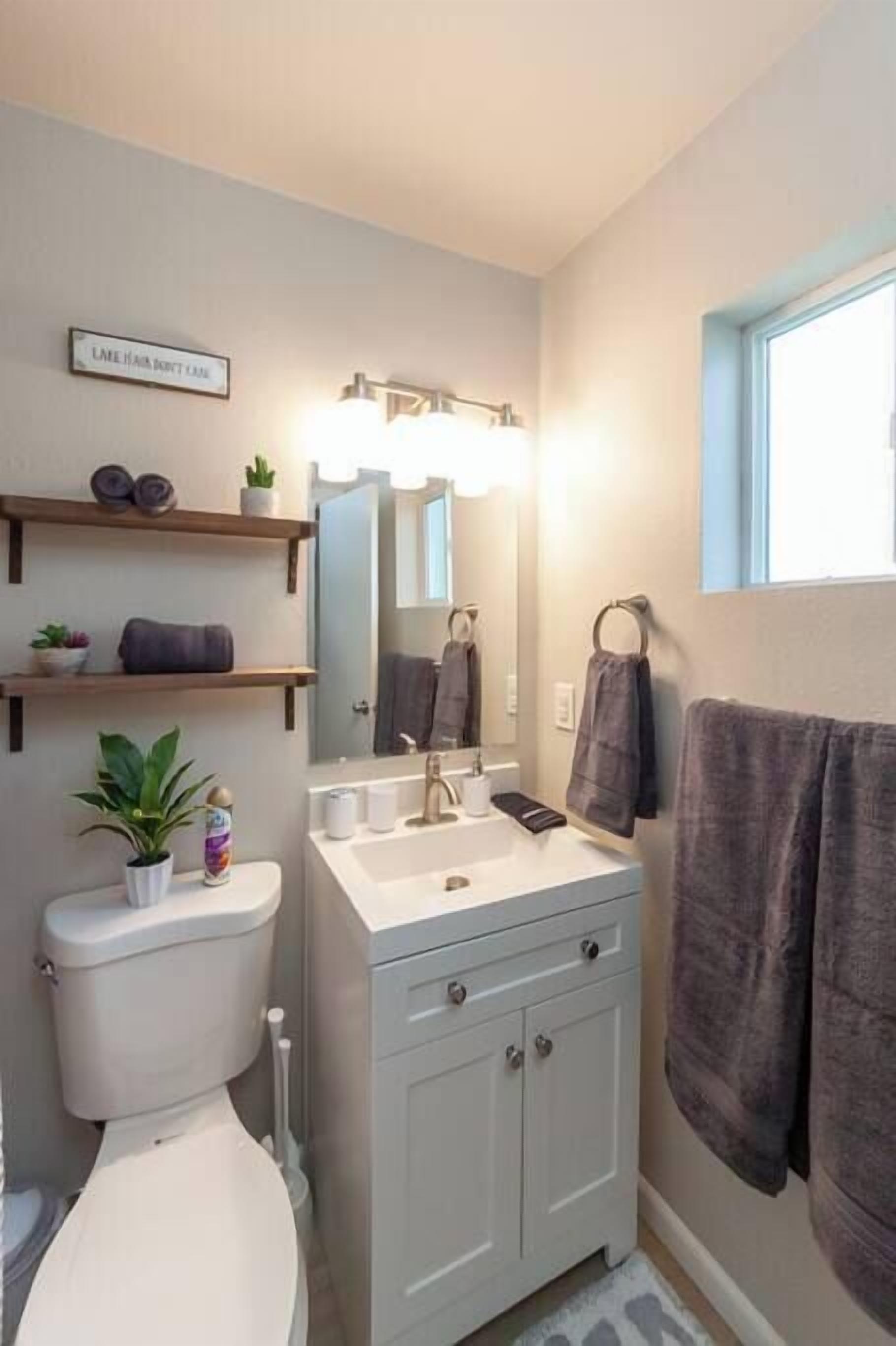 Ein Badezimmer mit Toilette, Waschbecken, Schrank, Spiegel, Handtuchhalter und einem Fenster.
