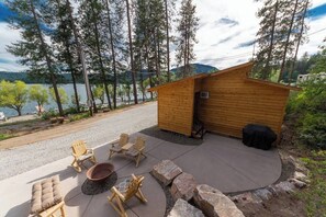Une cabane en bois dotée d’un patio en béton, entourée d’arbres et bordée par un lac.