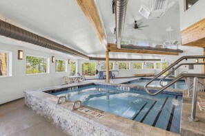 A swimming pool with clear lanes, a wooden ceiling, and a view of trees through large windows.