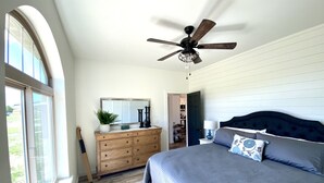 Un dormitorio con una cama grande, un ventilador de techo, un tocador y una ventana.