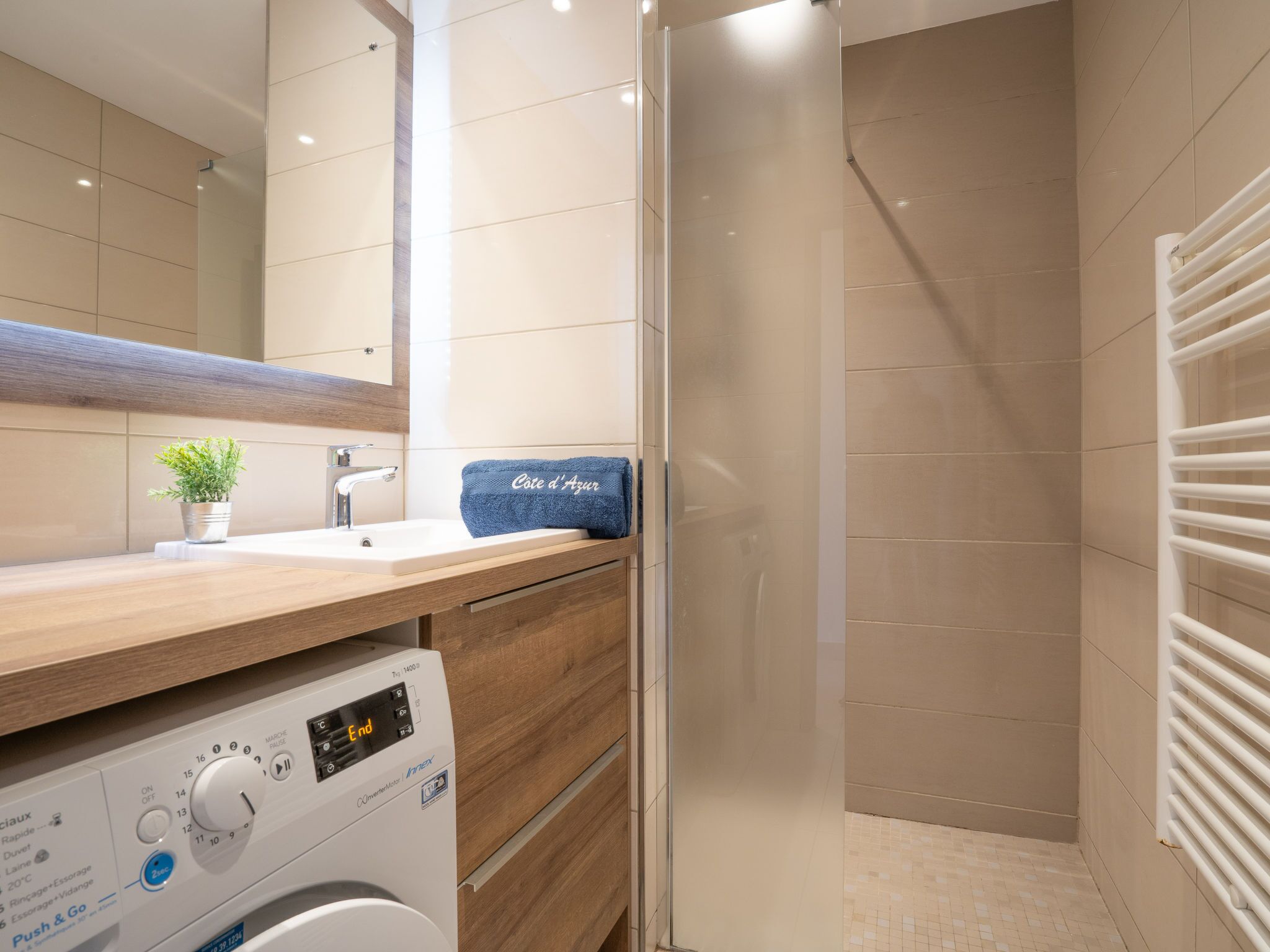 Ein modernes Badezimmer mit Duschkabine aus Glas, Waschbecken mit Handtuch und einer Waschmaschine.
