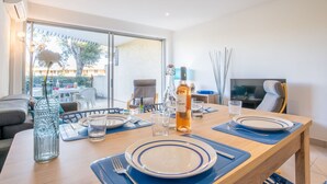 Un coin repas avec une table dressée pour deux personnes, une bouteille de vin et un vase avec une fleur.