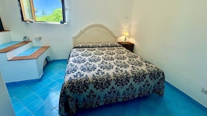 Une chambre à coucher avec un lit, une table de chevet, une fenêtre et un sol recouvert de carreaux bleus.
