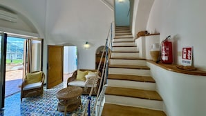 Un intérieur spacieux avec un escalier menant à un deuxième étage, des meubles en osier et un extincteur fixé au mur.