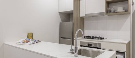 A modern kitchen with white cabinetry, a stainless steel sink, a built-in oven, and a small shelf with glassware.