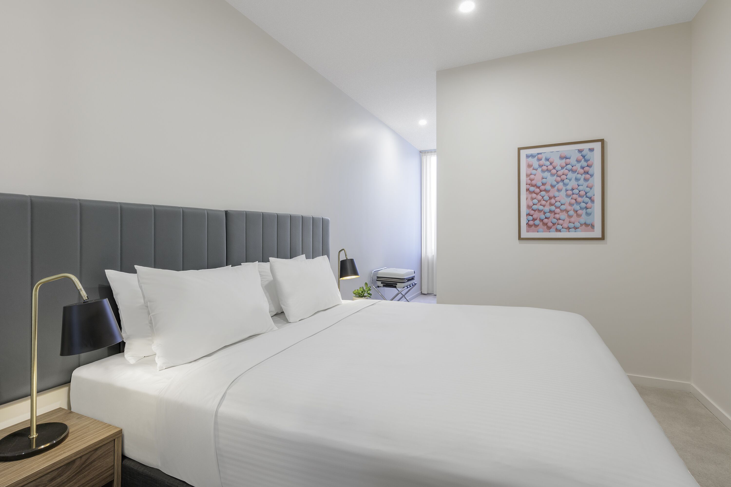 Une chambre à coucher moderne avec un grand lit, une table de chevet avec une lampe et une œuvre d’art encadrée accrochée au mur.