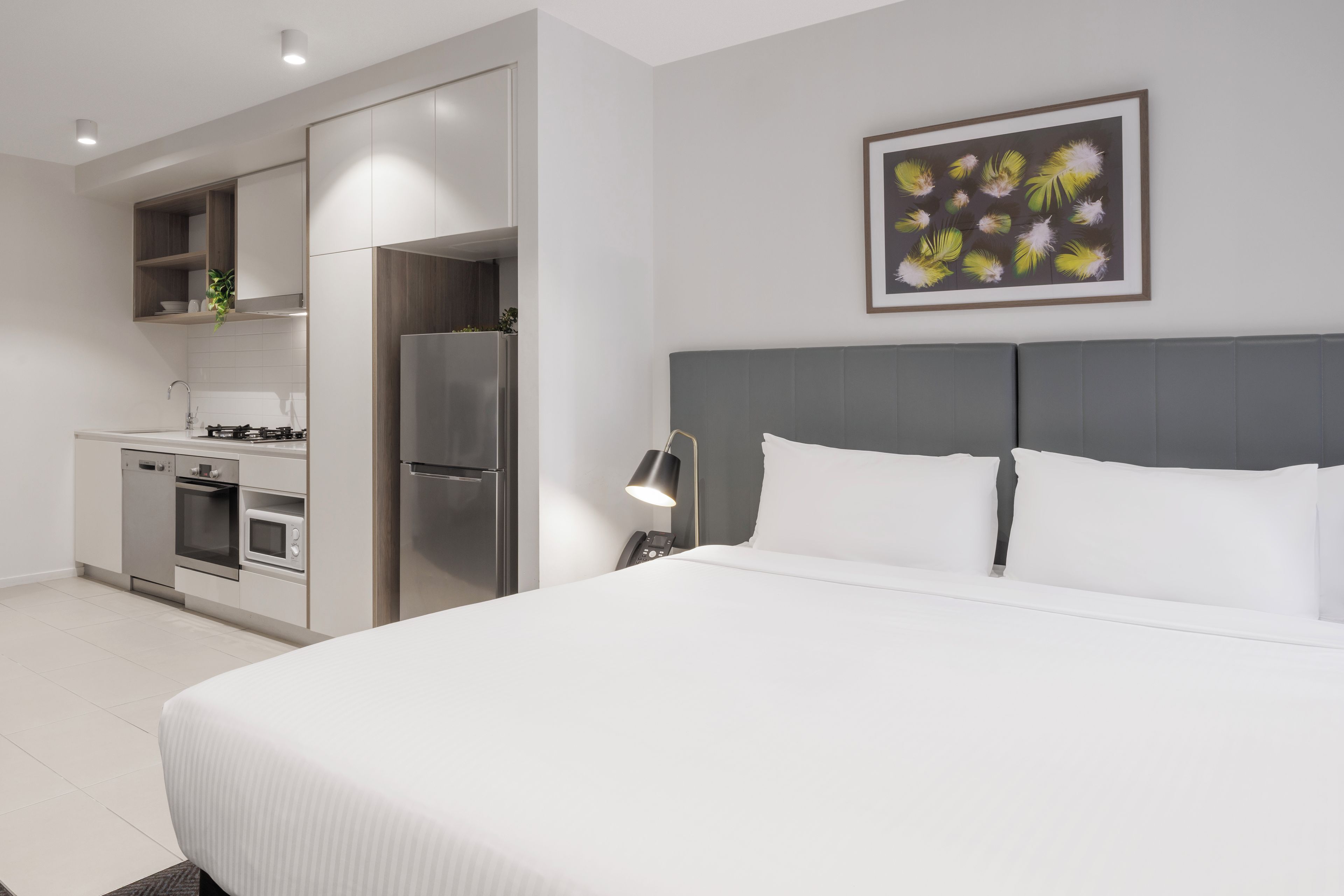 Een moderne hotelkamer met een groot bed, een kitchenette en een schilderij aan de muur.