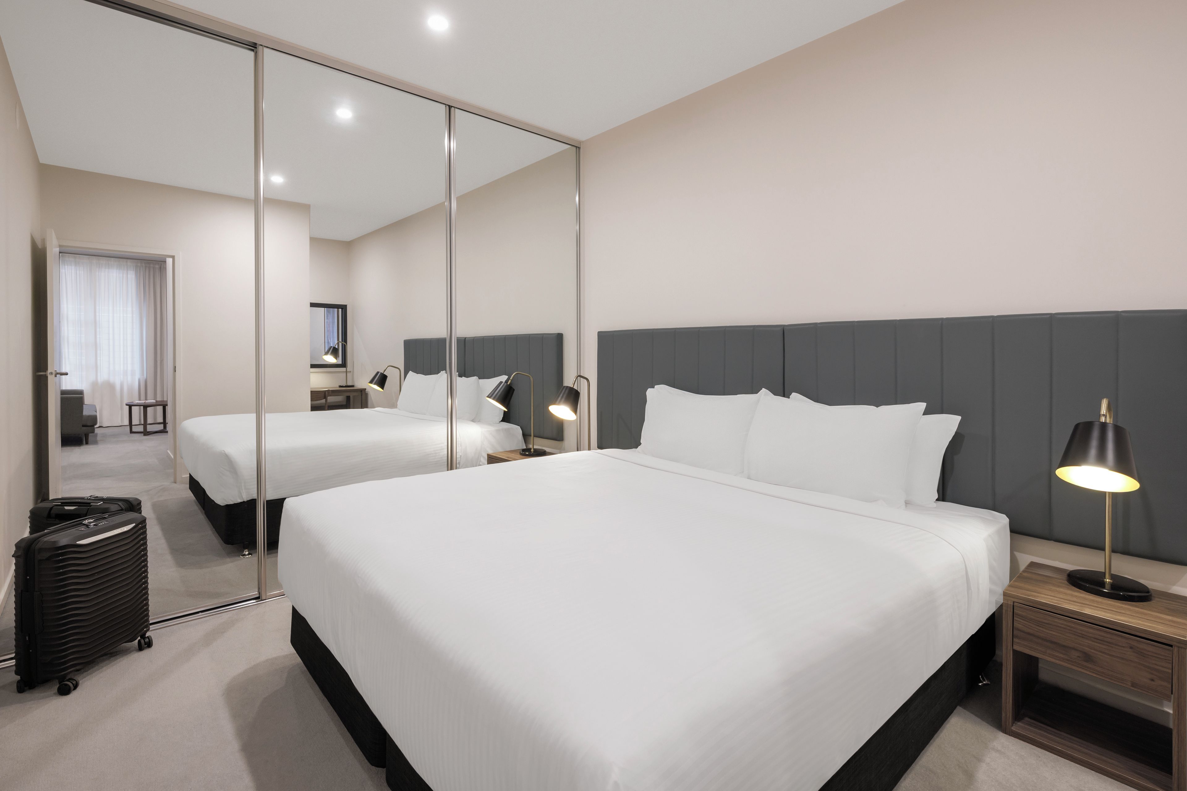 Una camera d'albergo con due letti, un grande specchio e un comodino con una lampada.