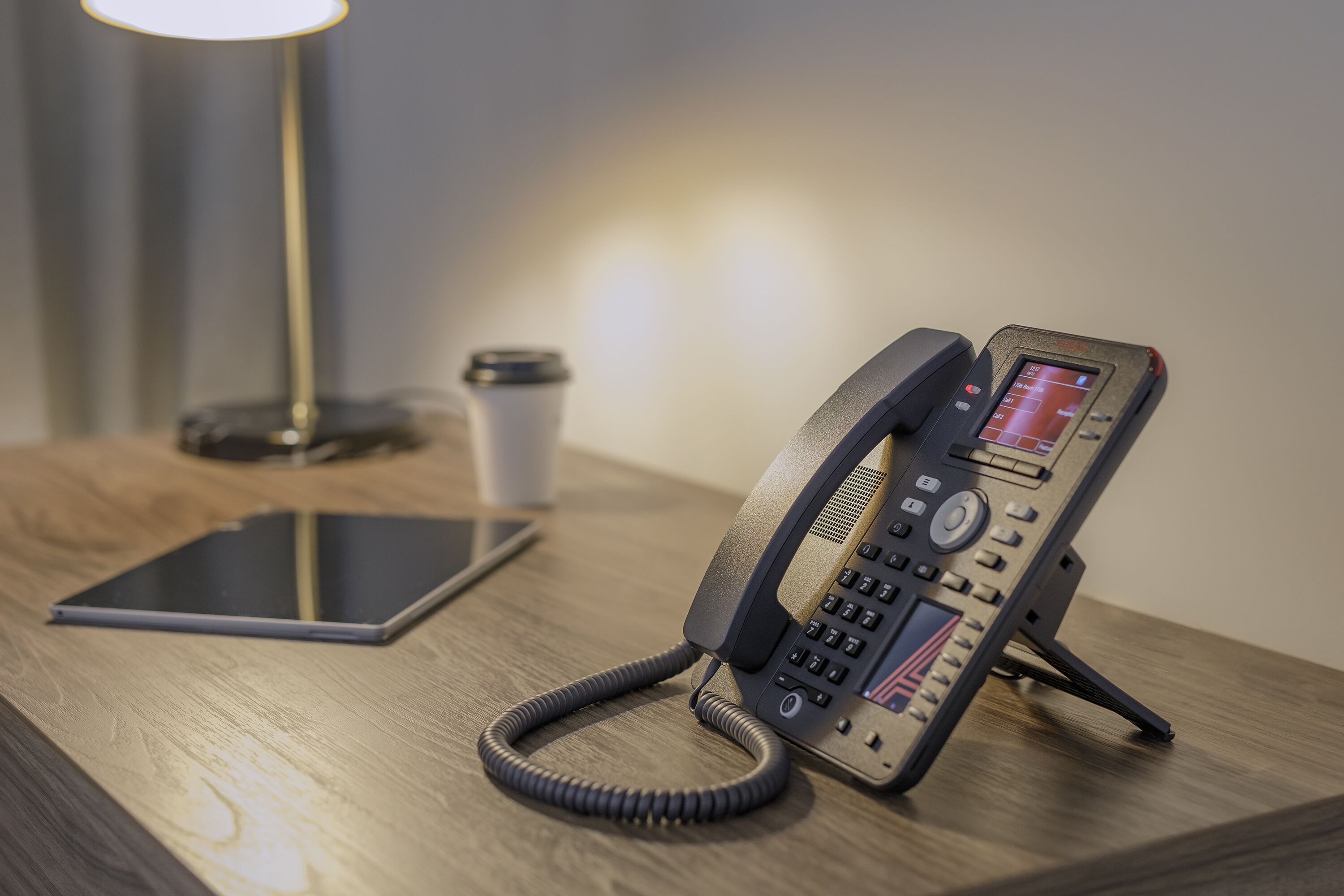 Un escritorio con un teléfono fijo, una tableta y una taza de café.