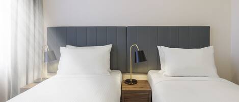 A hotel room with two beds, a nightstand with a lamp, and a window with curtains.