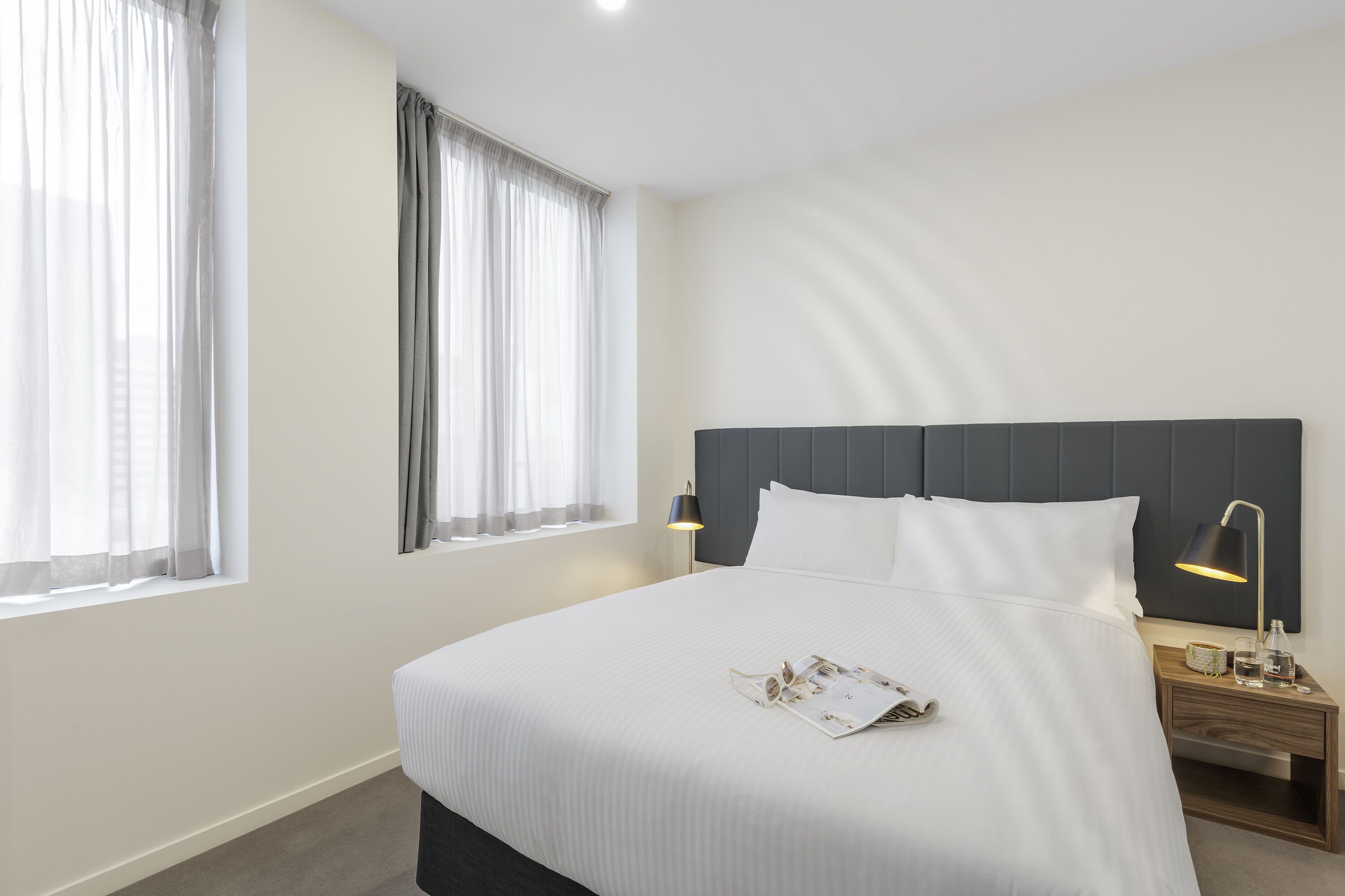 A neatly made bed with white linens, a dark headboard, and a bedside table with a lamp.