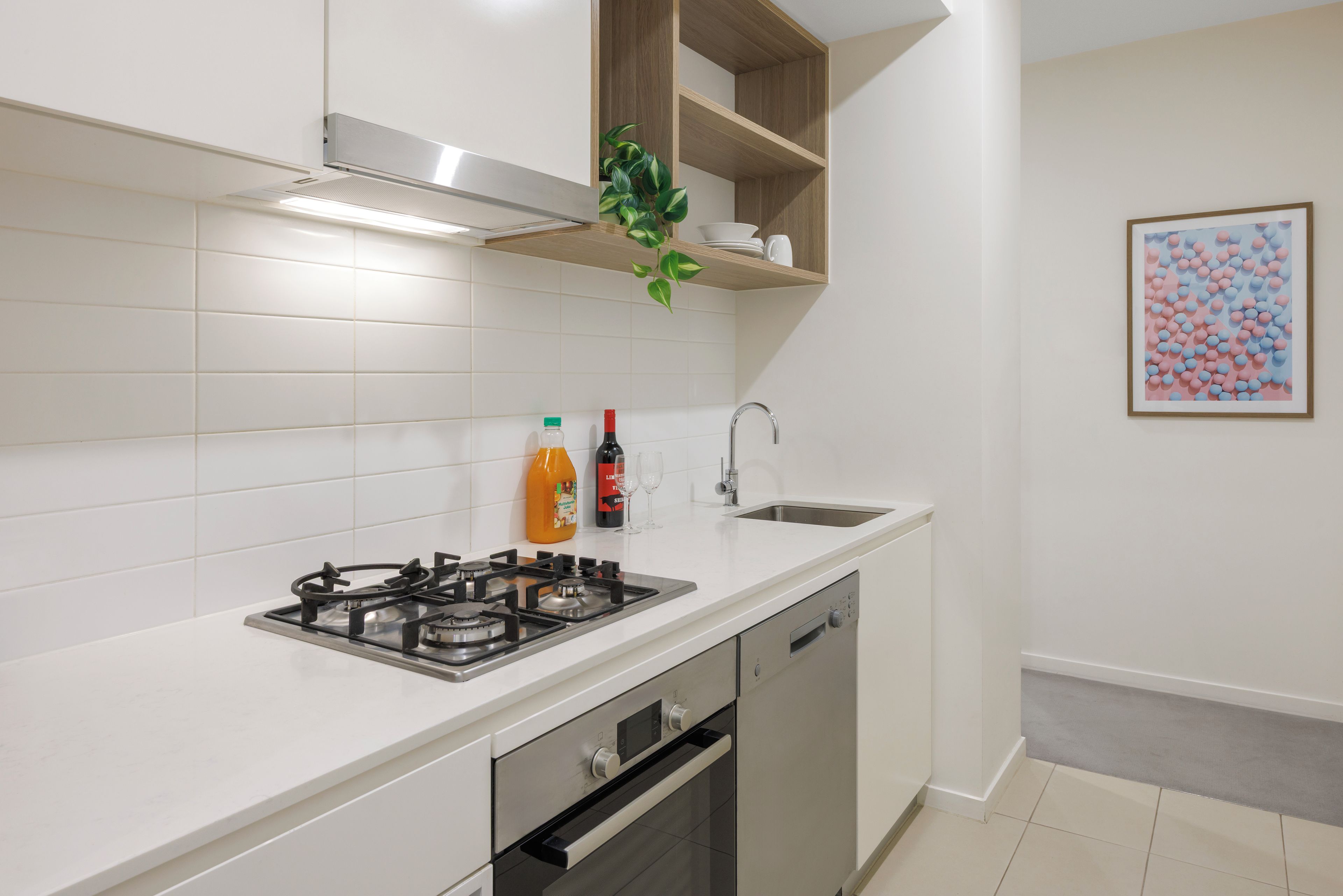 Cozinha moderna com armários brancos, fogão a gás, forno embutido e pia de aço inoxidável.
