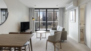 A modern living room with a dining table, sofa, and TV. It features large windows with a city view. - Brady Apartment Hotel Hardware Lane (Melbourne)