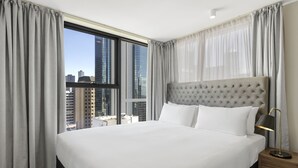 A hotel room with a large bed, a nightstand, a lamp, and a view of the cityscape through large windows. - Brady Apartment Hotel Hardware Lane (Melbourne)