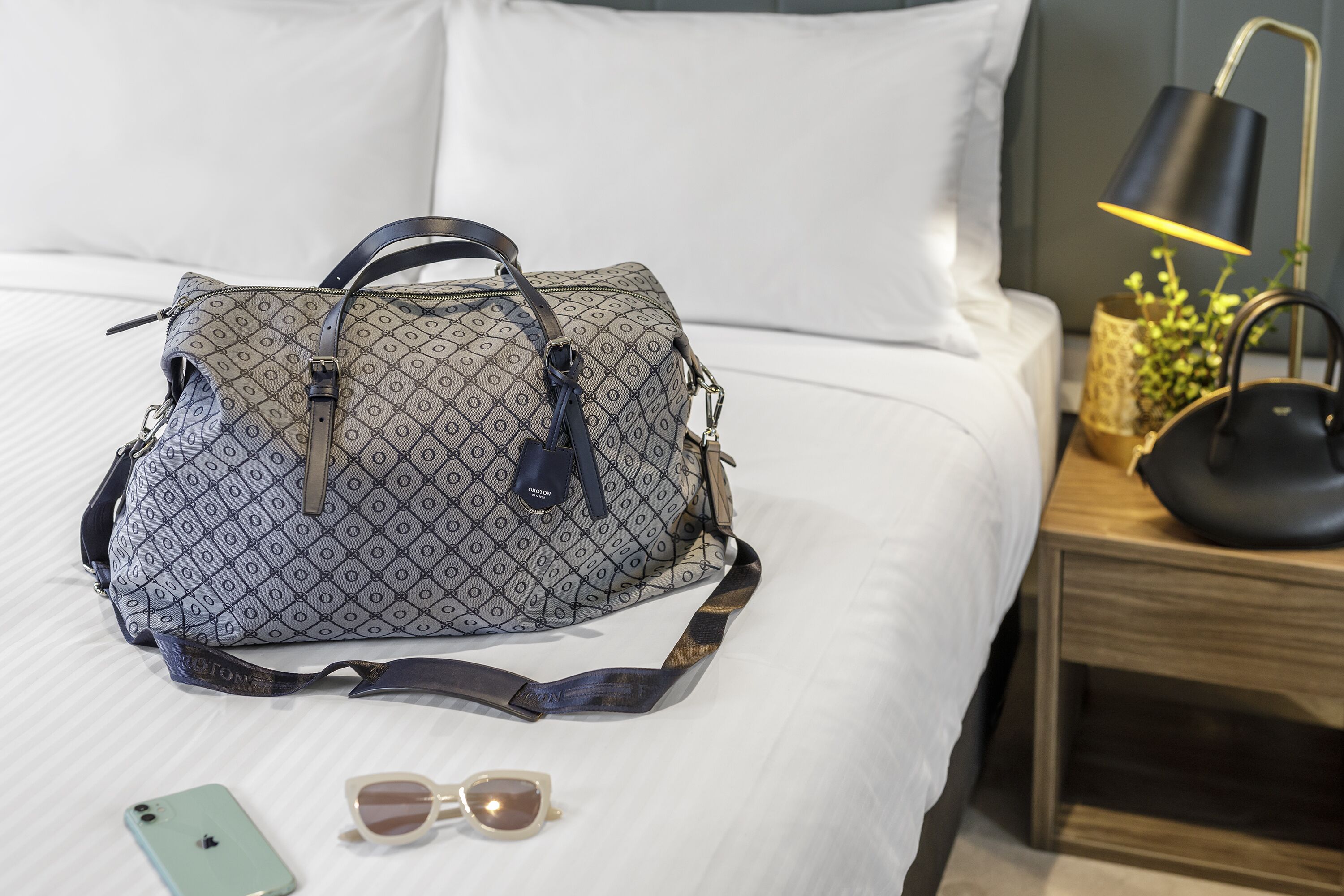 A bed with a patterned bag, sunglasses, and a phone on it.