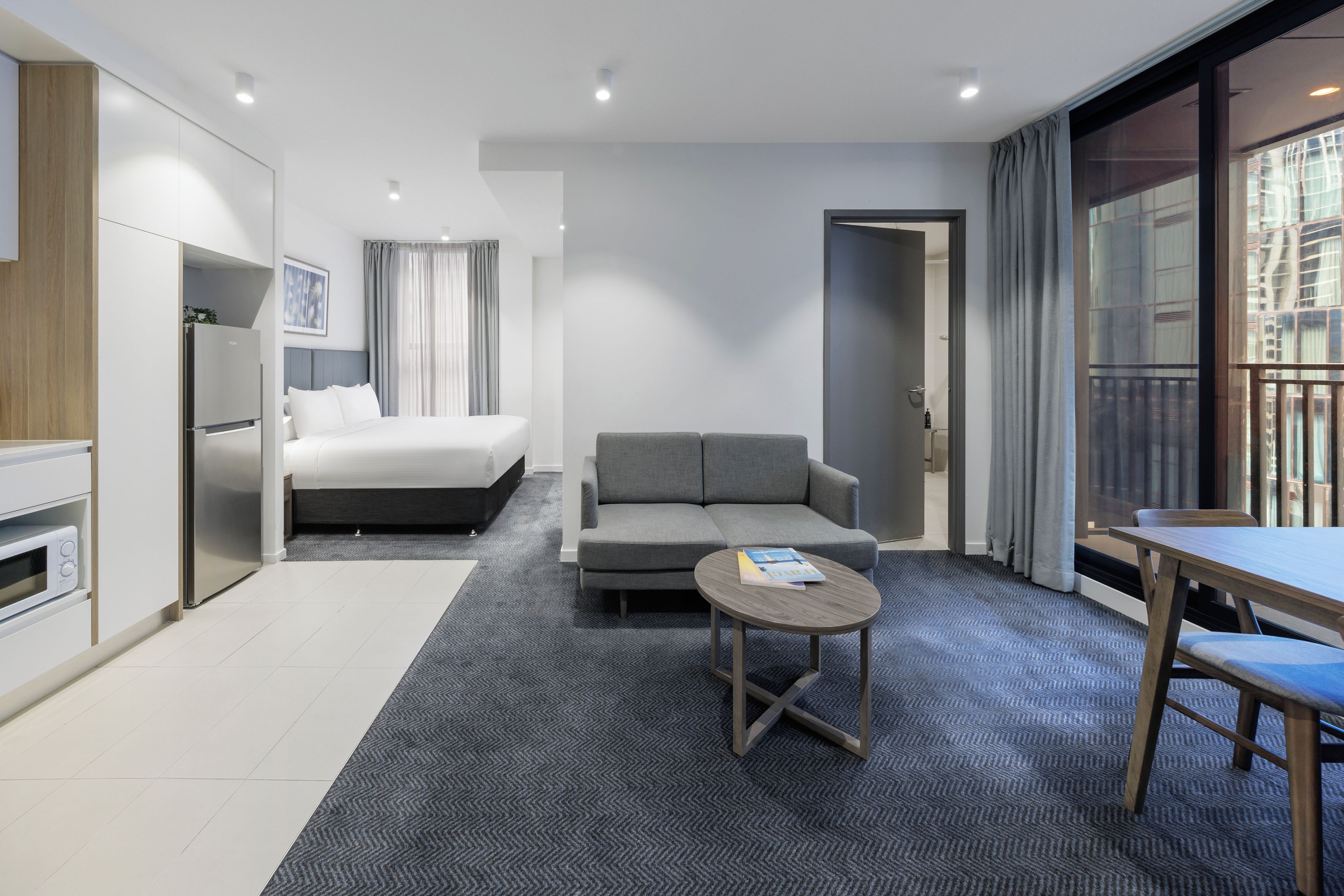 A modern hotel room with a bed, sofa, dining table, and a small coffee table.