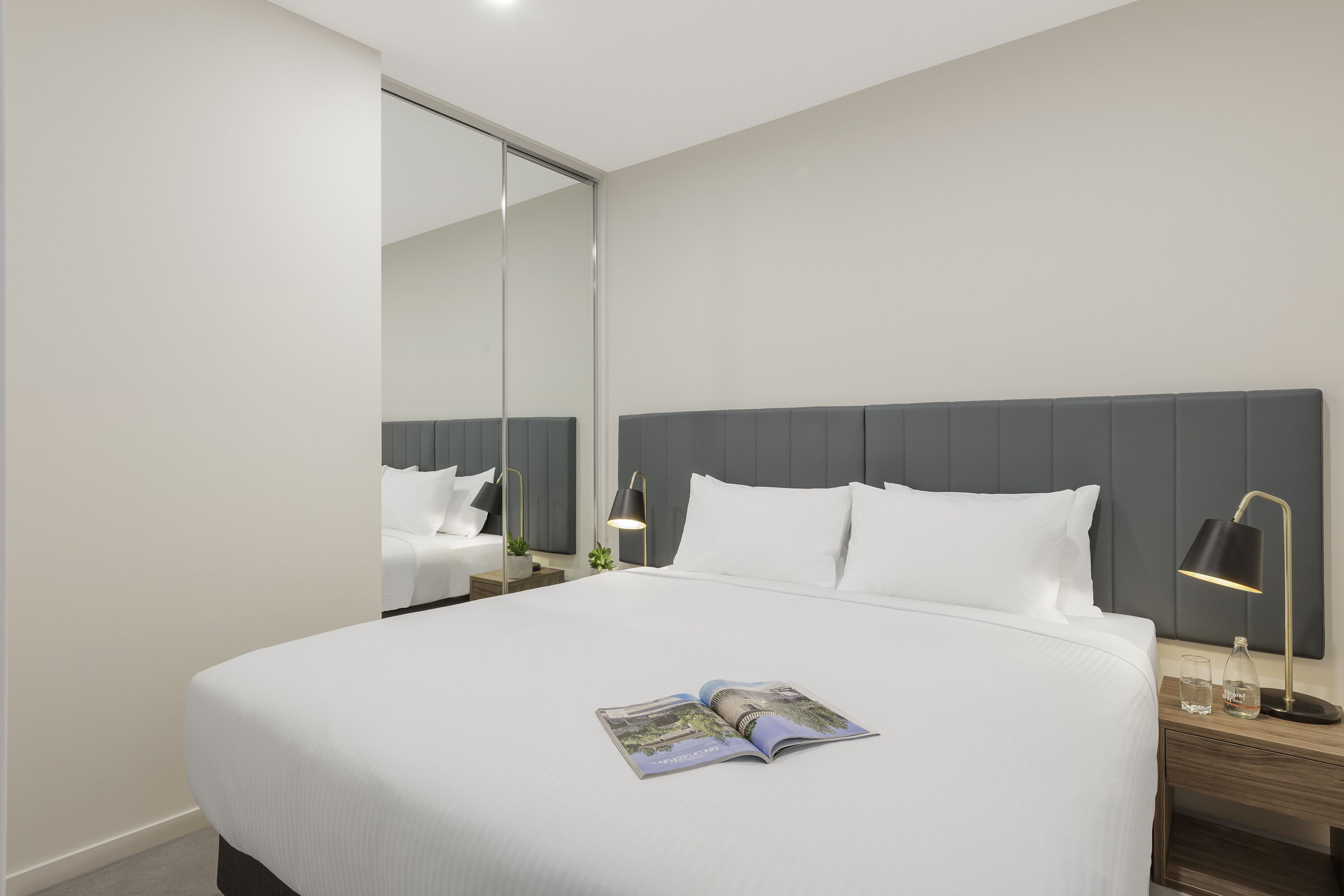 Une chambre d’hôtel moderne avec un grand lit, une table de chevet avec une lampe et un miroir.
