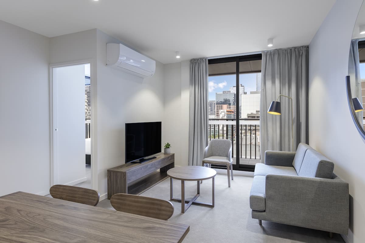 Una sala de estar moderna con televisor de pantalla plana, sofá gris y una mesa de comedor.