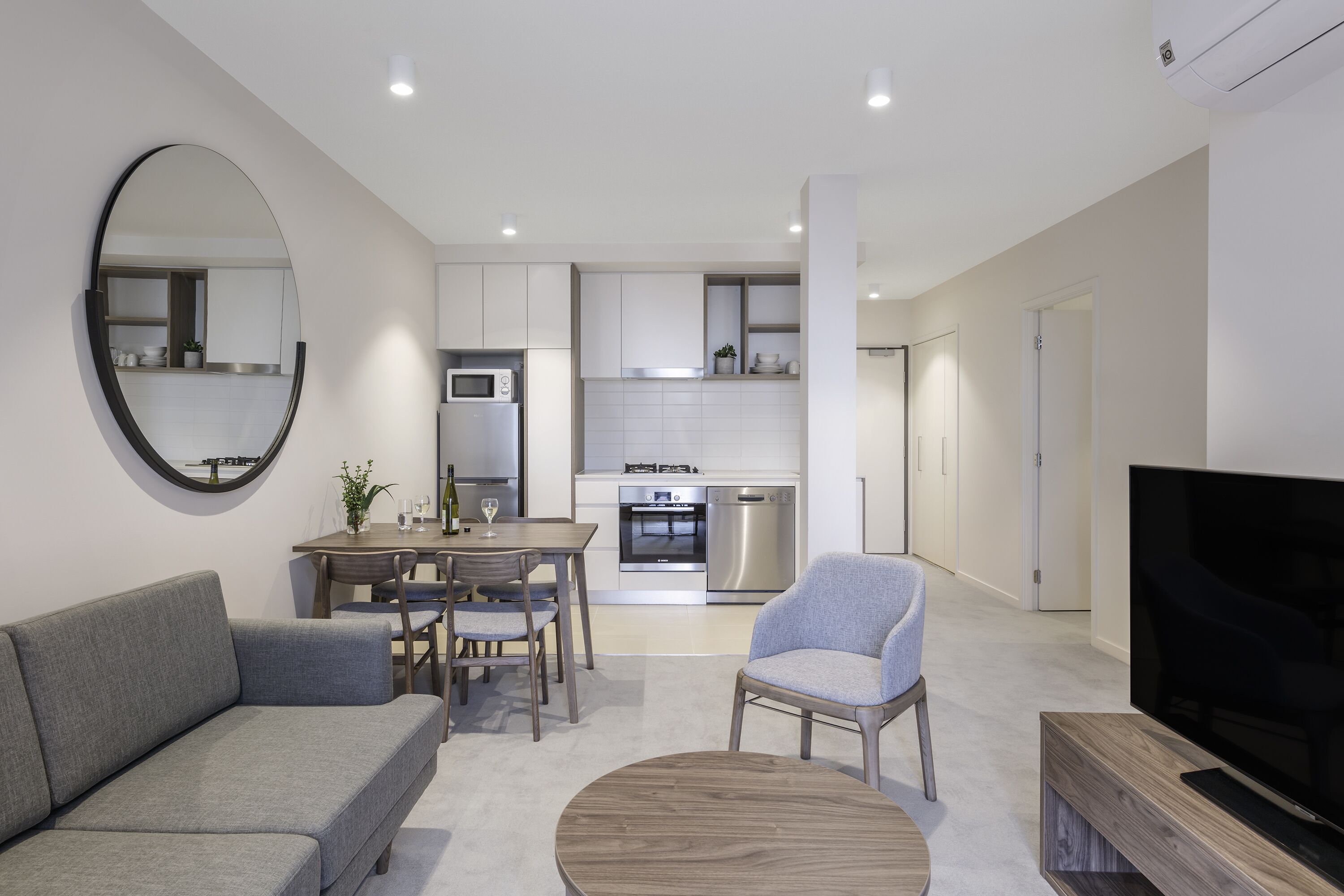 A modern living room with a grey sofa, a round coffee table, a TV, and a dining area with a table and chairs.
