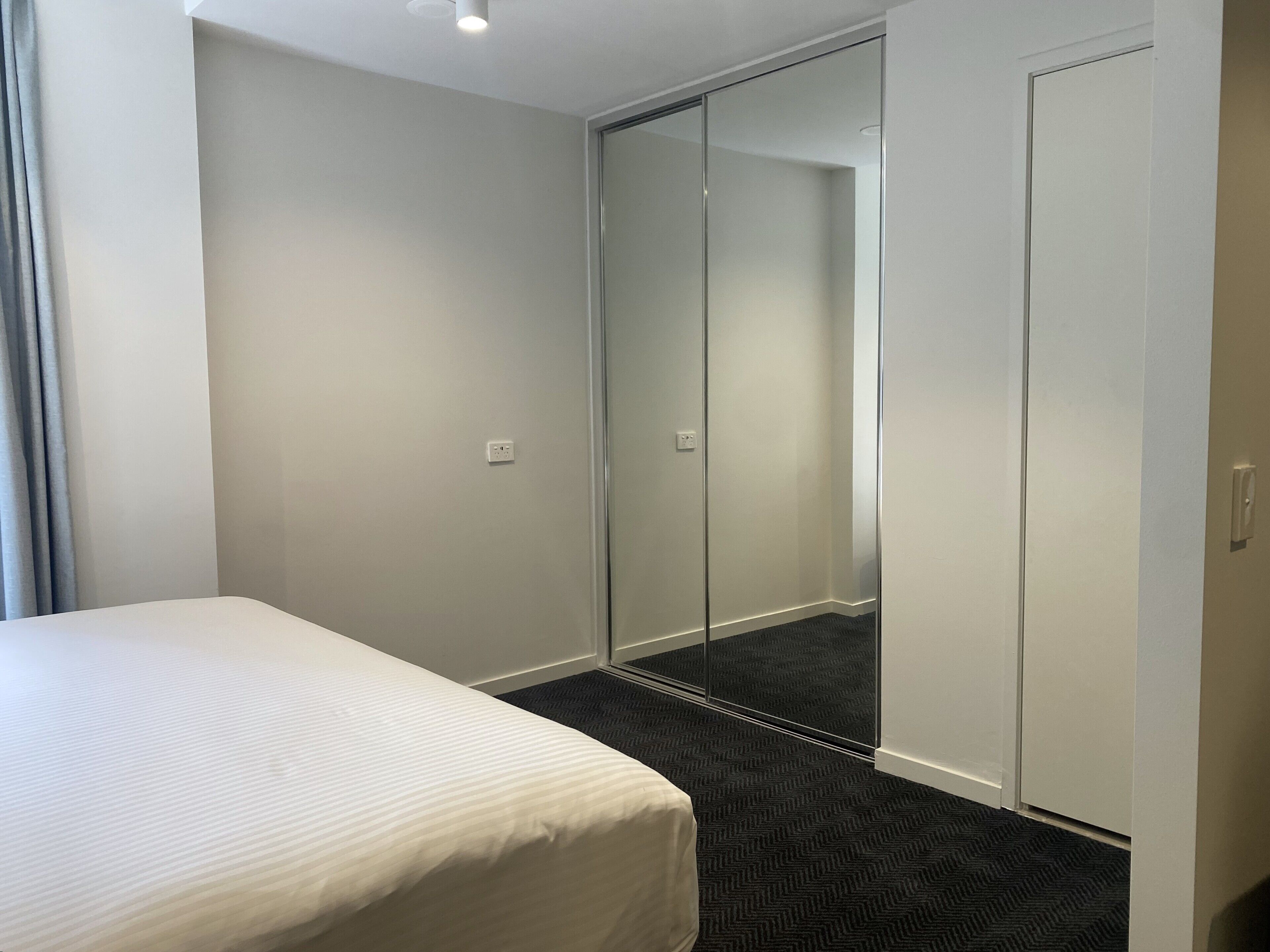 A hotel room with a bed, a walk-in closet, and a carpeted floor.