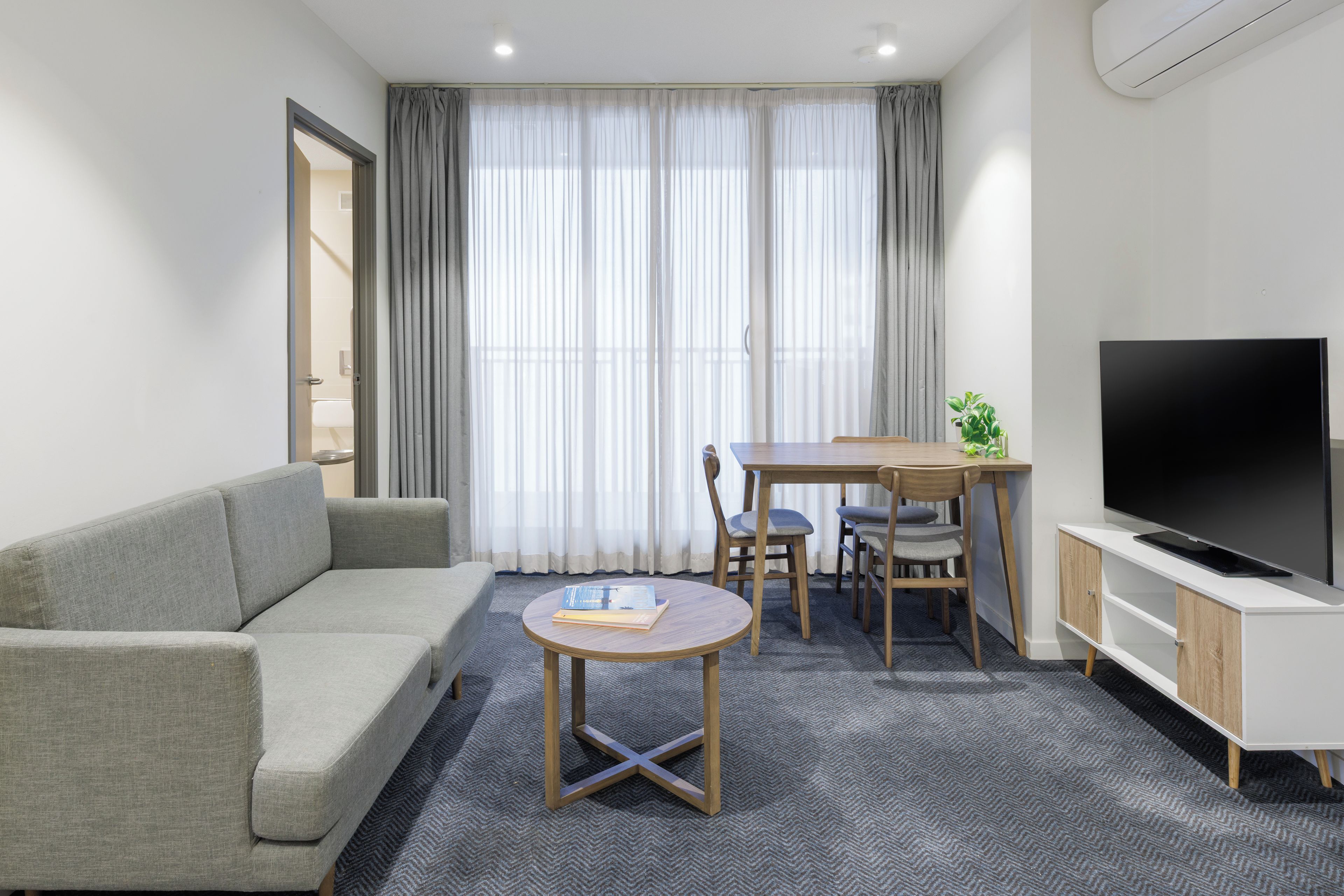 A modern living room with a sofa, a dining table with chairs, a TV, and a small table with a book.