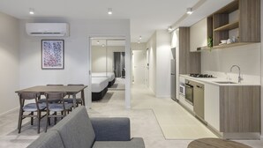 A modern apartment with a dining area, a sofa, a kitchen with wooden cabinets, and a hallway leading to a bedroom. - Brady Apartment Hotel Hardware Lane (Melbourne)