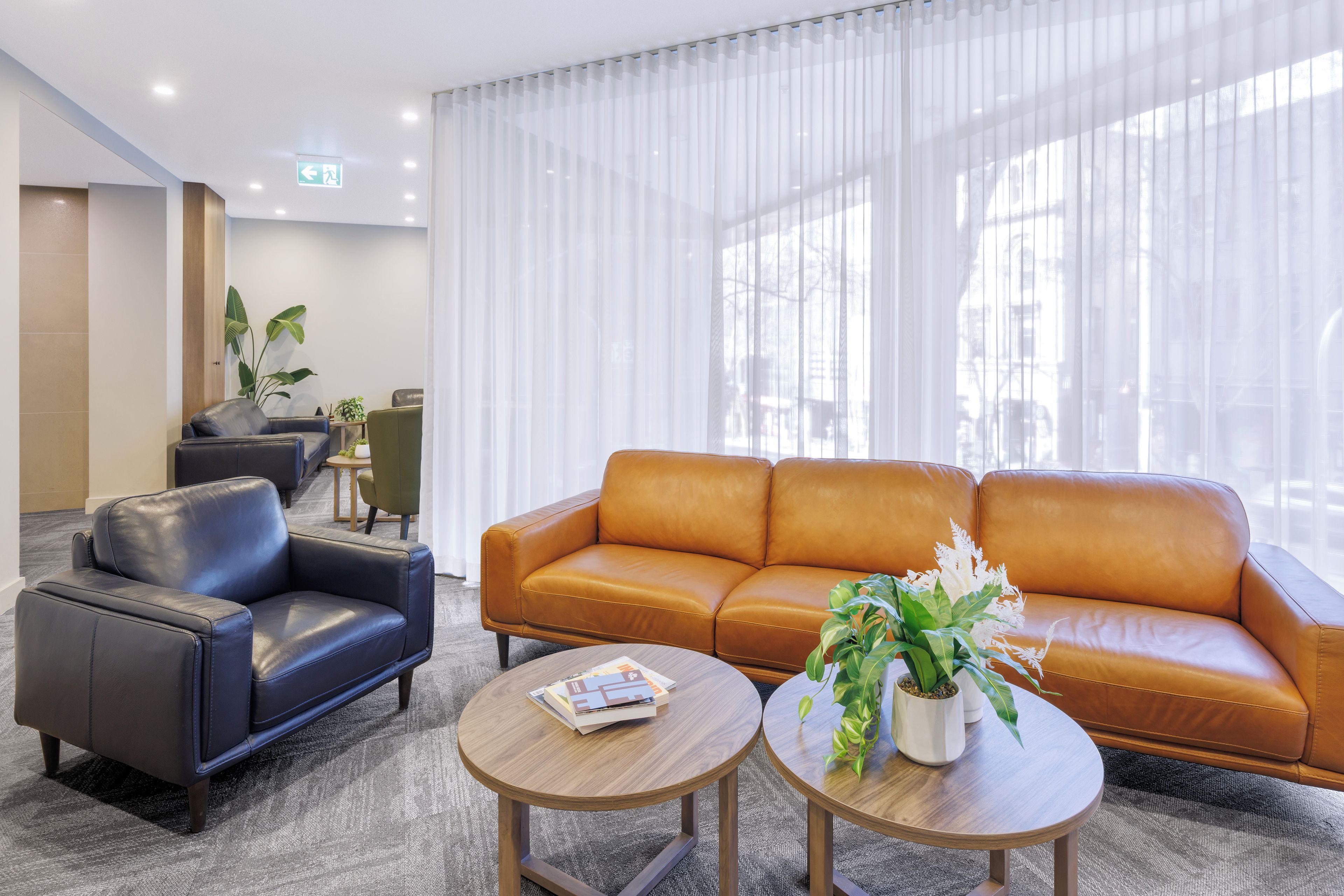 A modern lobby with a leather sofa, a black armchair, and a round wooden table with magazines.