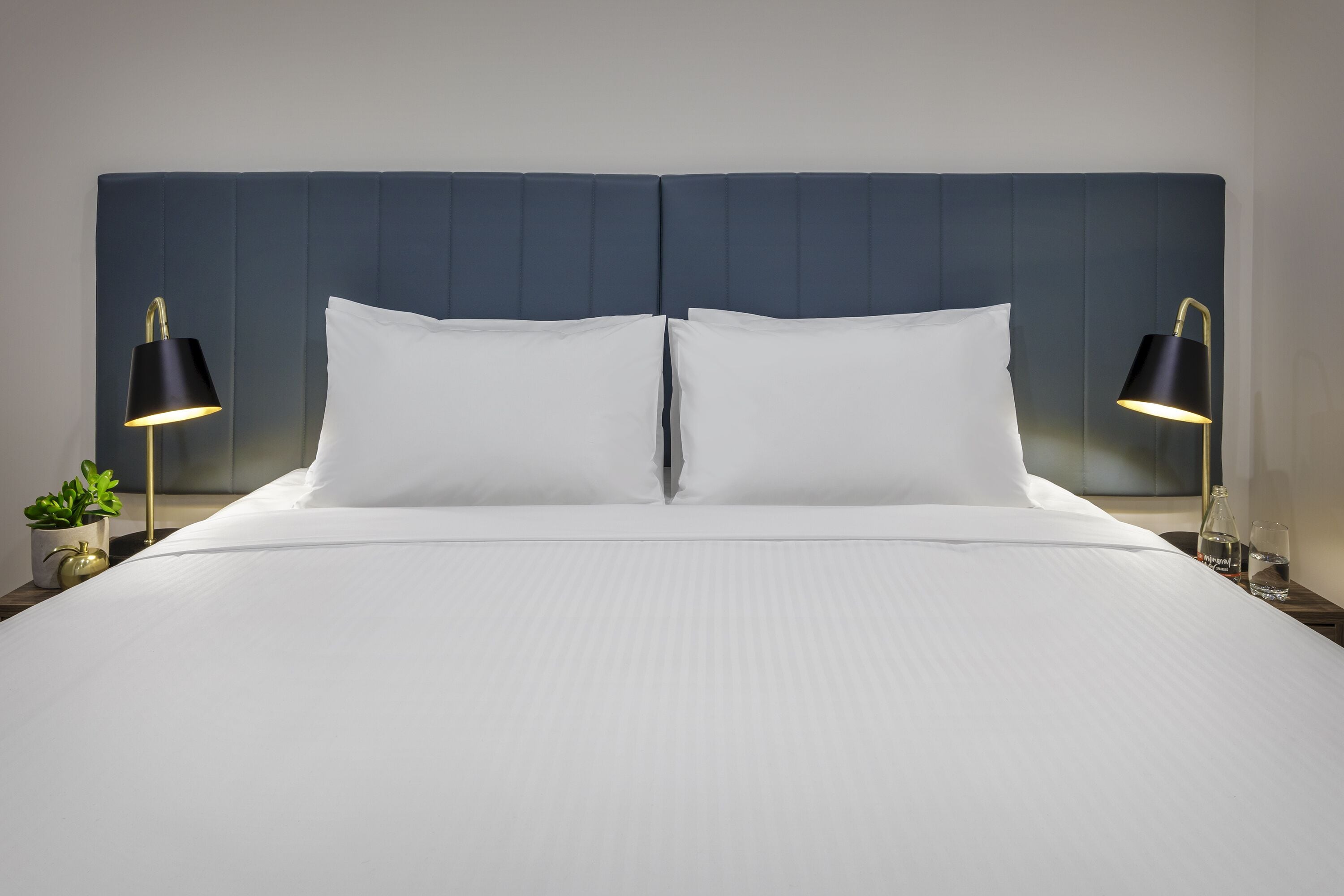 A neatly made bed with white linens, flanked by two black bedside lamps, and a dark blue headboard.