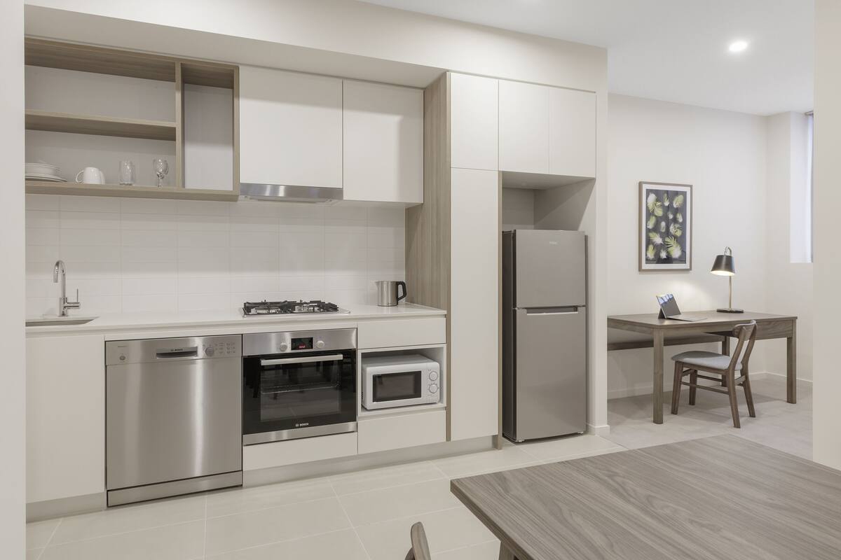Una cocina moderna con electrodomésticos integrados, una zona de comedor con mesa y sillas, y un cuadro enmarcado en la pared.