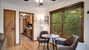 Un comedor acogedor con una mesa redonda y dos sillas, un ventilador de techo de madera y un ventanal con vistas a la vegetación.