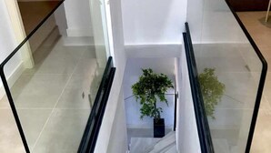 A modern staircase with glass railings, leading to a landing with a potted plant. - LAS GAVIOTAS 9A APARTMENT (Tarifa)