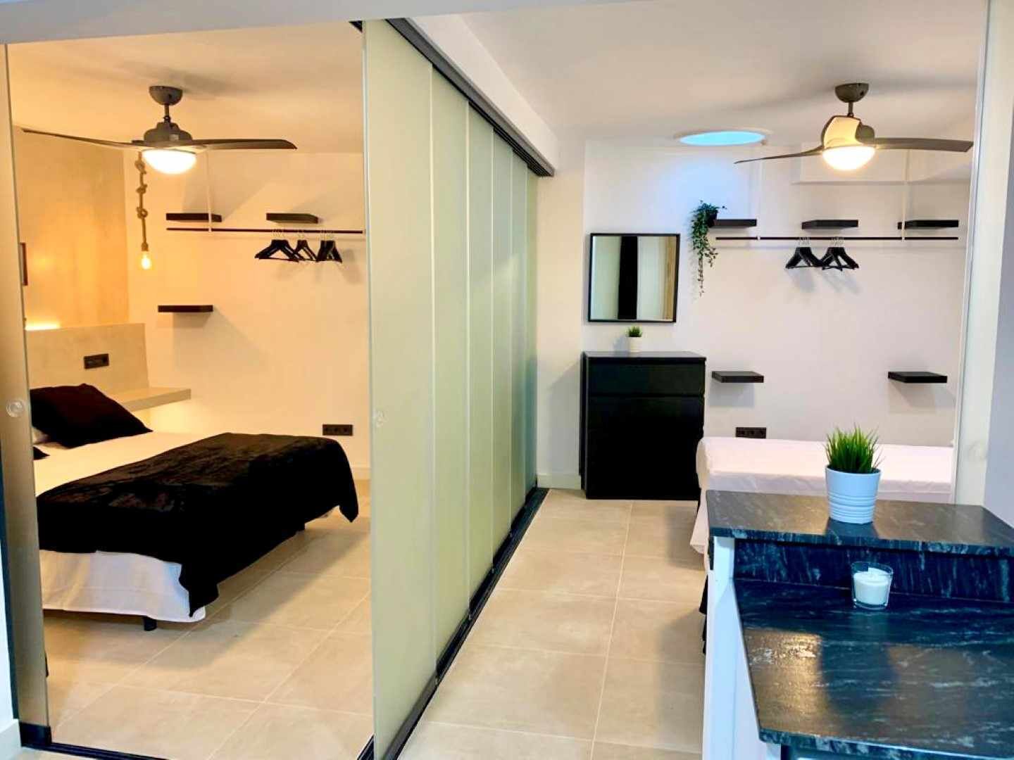 A modern hotel room with a bed, bedside tables, a dresser, a mirror, and a small plant.
