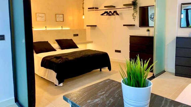 A modern bedroom with a bed, a ceiling fan, a bedside table, and a potted plant. - LAS GAVIOTAS 9B APARTMENT (Tarifa)