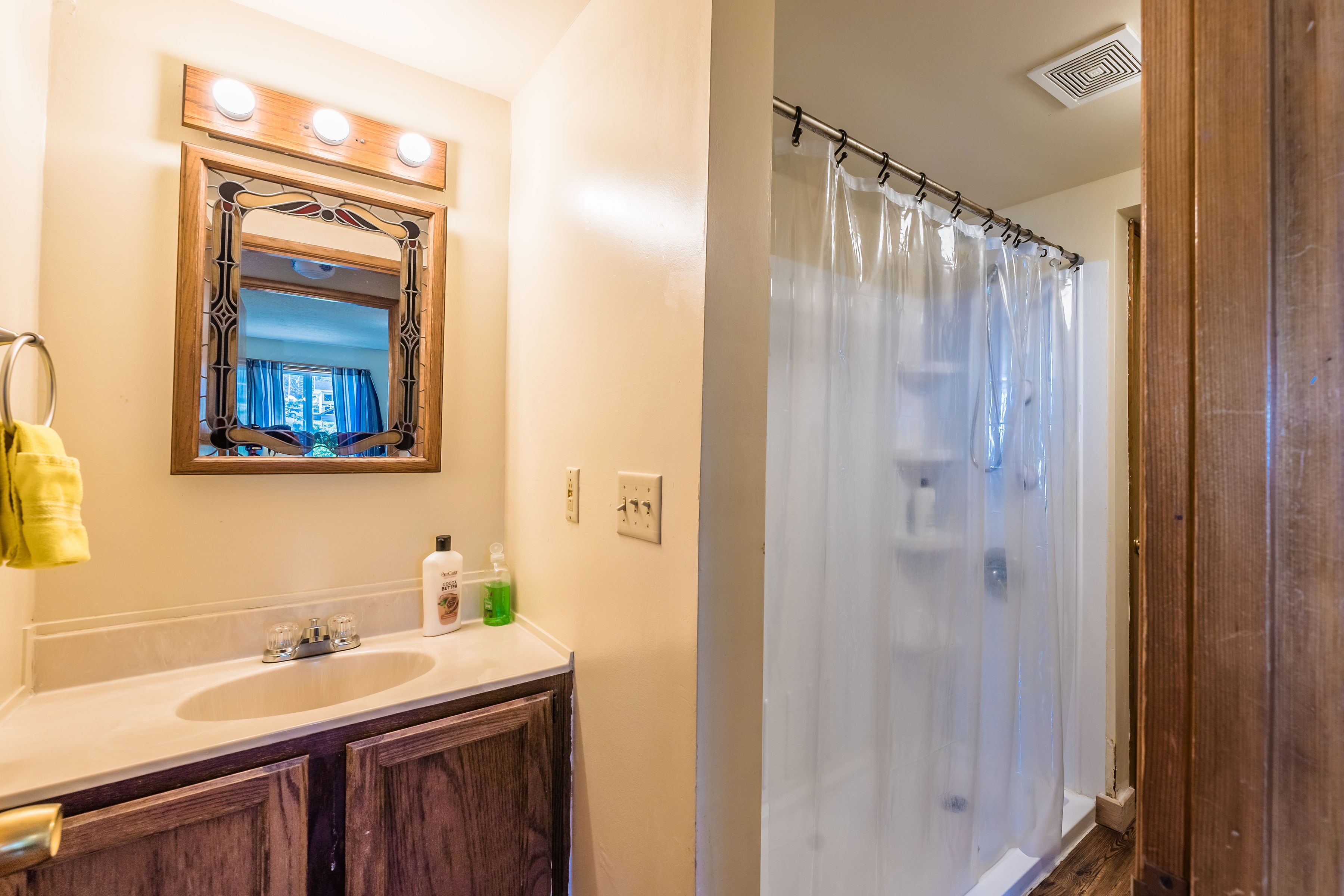 A bathroom with a double sink, a mirror with lights, and a shower curtain.