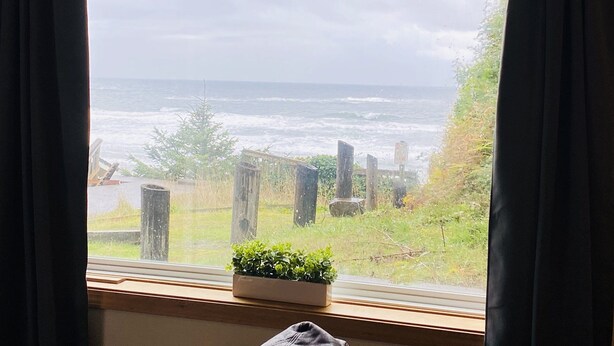 A room with a large window overlooking the ocean, a wooden bench, and a potted plant.