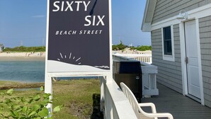 Señal de 'Sixty Six Beach Street' con vista a la playa y un edificio al fondo.