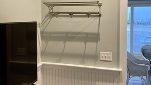 Una habitación con aire acondicionado, un televisor sobre un mueble, una estantería metálica y un enchufe.