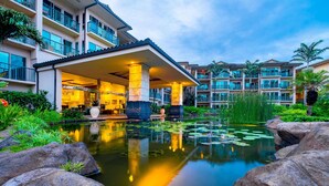 A hotel with a pool surrounded by rocks and plants, a covered entrance, and multiple balconies. - Enjoy Perfect Vacation at Luxury Beach Front Resort. (Kapaʻa)
