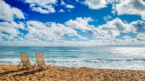 A beach with two empty lounge chairs facing the ocean under a partly cloudy sky. - Enjoy Perfect Vacation at Luxury Beach Front Resort. (Kapaʻa)