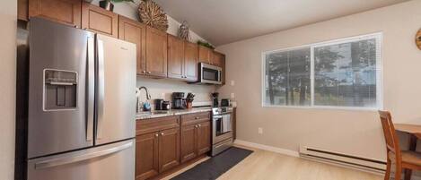 A modern kitchen with stainless steel appliances, wooden cabinets, and a window with blinds.