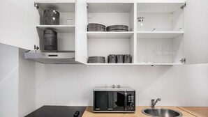A compact kitchen with a built-in microwave, a sink, and open shelving above the countertop. - Exclusive Kohlmarkt 1 BR w/ Elevator, walk to Metro U1, U3, by Blueground (Vienna)