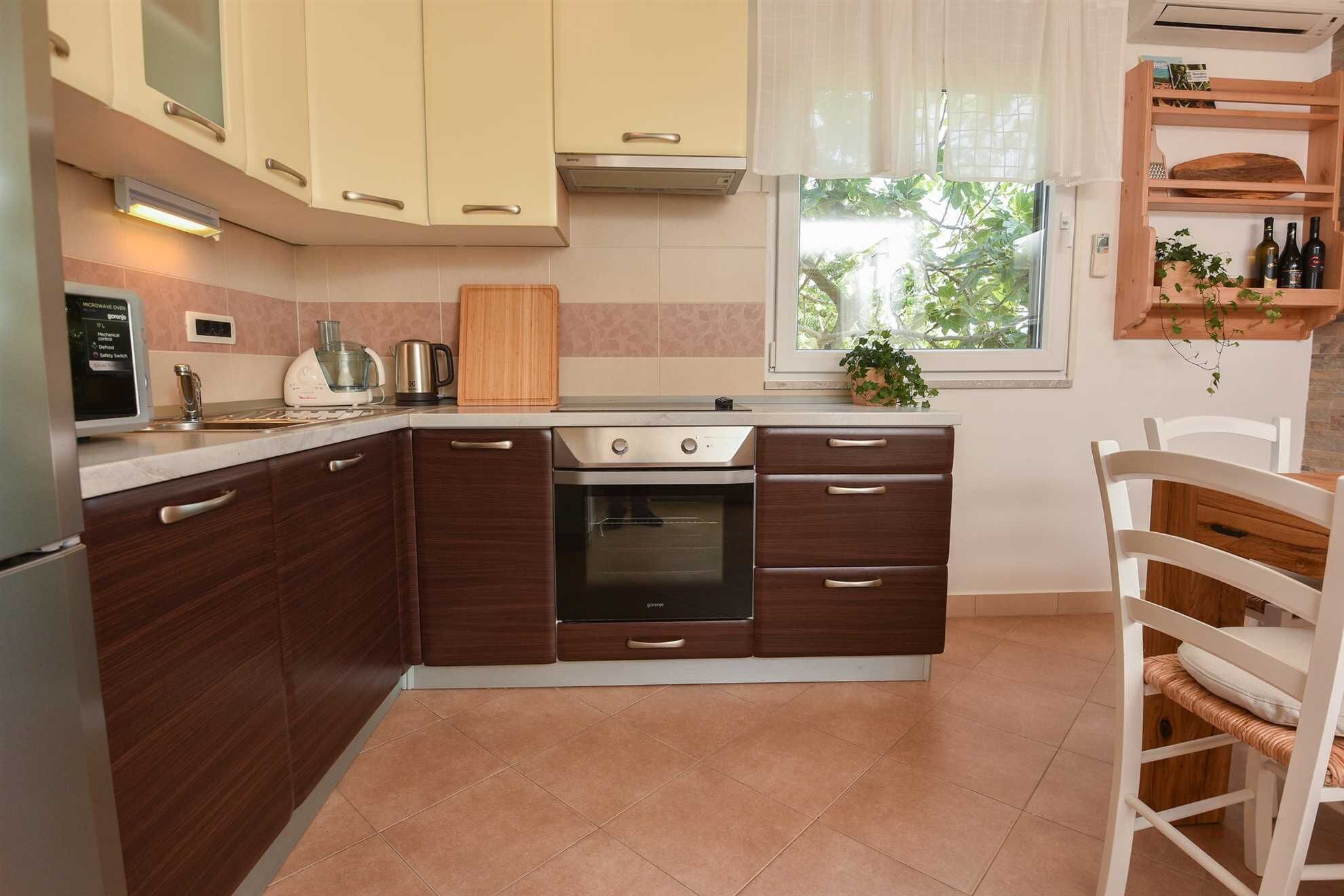 A compact kitchen with a stove, microwave, and sink. There is a window with a view of greenery outside.