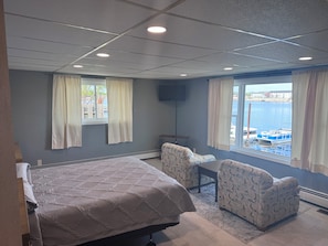 A bedroom with a bed, two armchairs, a TV, and a window with a view of the sea. - River Front Property (La Crosse)
