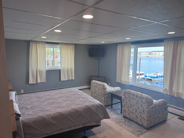 Une chambre à coucher avec un lit, deux fauteuils, un téléviseur et une fenêtre donnant sur la mer.