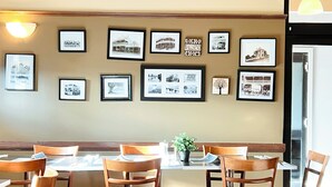 A dining area with a long table and multiple chairs, framed photographs on the wall, and a small potted plant. - Colliery Inn, Wallsend (Wallsend)