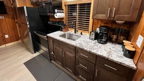 A modern kitchen with wooden cabinets, a stainless steel refrigerator, a built-in oven, a sink, and a coffee maker.