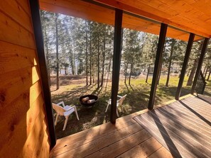 A wooden deck with a fire pit and chairs, overlooking a forested area. - Rustic 1 bd, 1 ba Cabin at Waitts Lake Resort! (Valley)