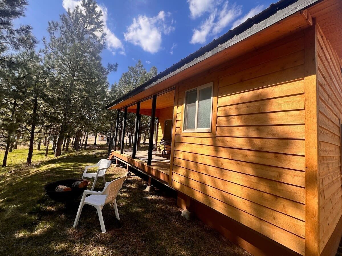 Une cabane en bois dotée d’un porche, entourée d’arbres.