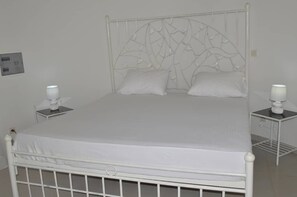 Una cama de metal blanco con un cabecero decorativo, dos mesitas de noche con lámparas y un colchón blanco.