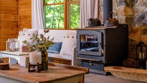 A cozy cabin interior with a stone fireplace, wooden furniture, and a view of greenery outside. - Cabin By The Creek! Inground Pool! Spa! (Dayton)